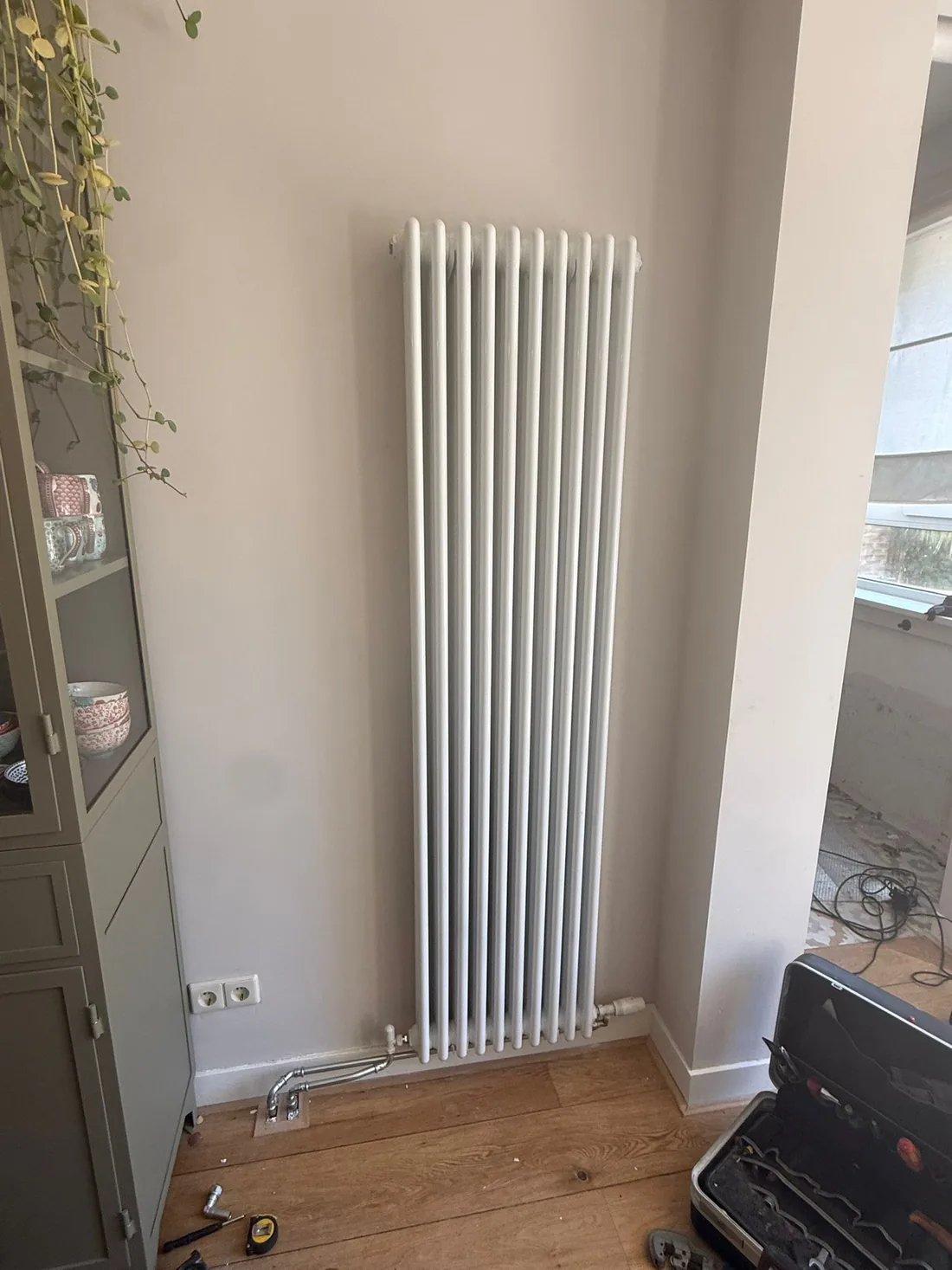 Verchroomde koperen leidingen komen uit de houten vloer naar de aansluiting van de kolomradiator