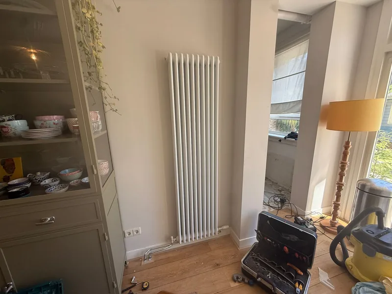 Witte verticale kolomradiator in de hoek van een woonkamer in een oud Amsterdams pand